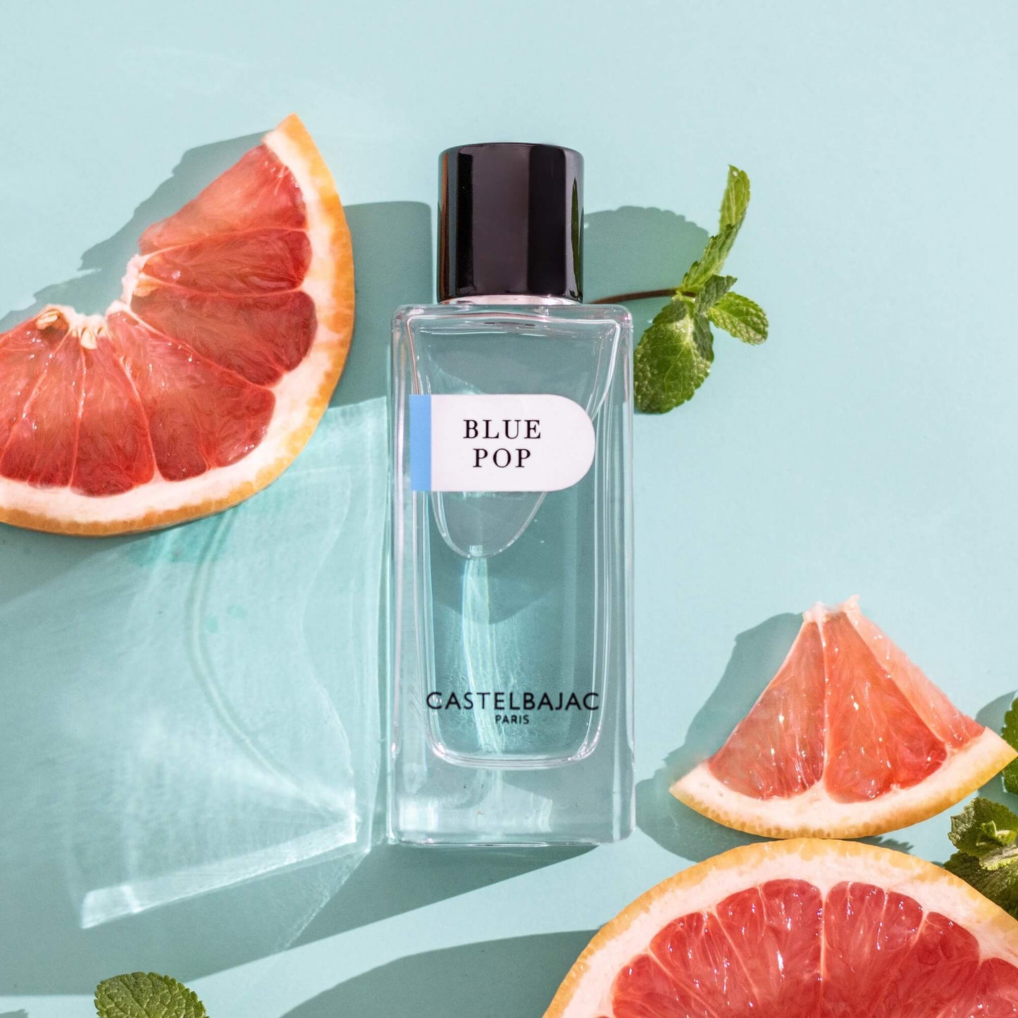 Castelbajac BLUE POP Eau de Parfum bottle with vibrant blue liquid, set against a backdrop of Mediterranean cliffs and turquoise waves