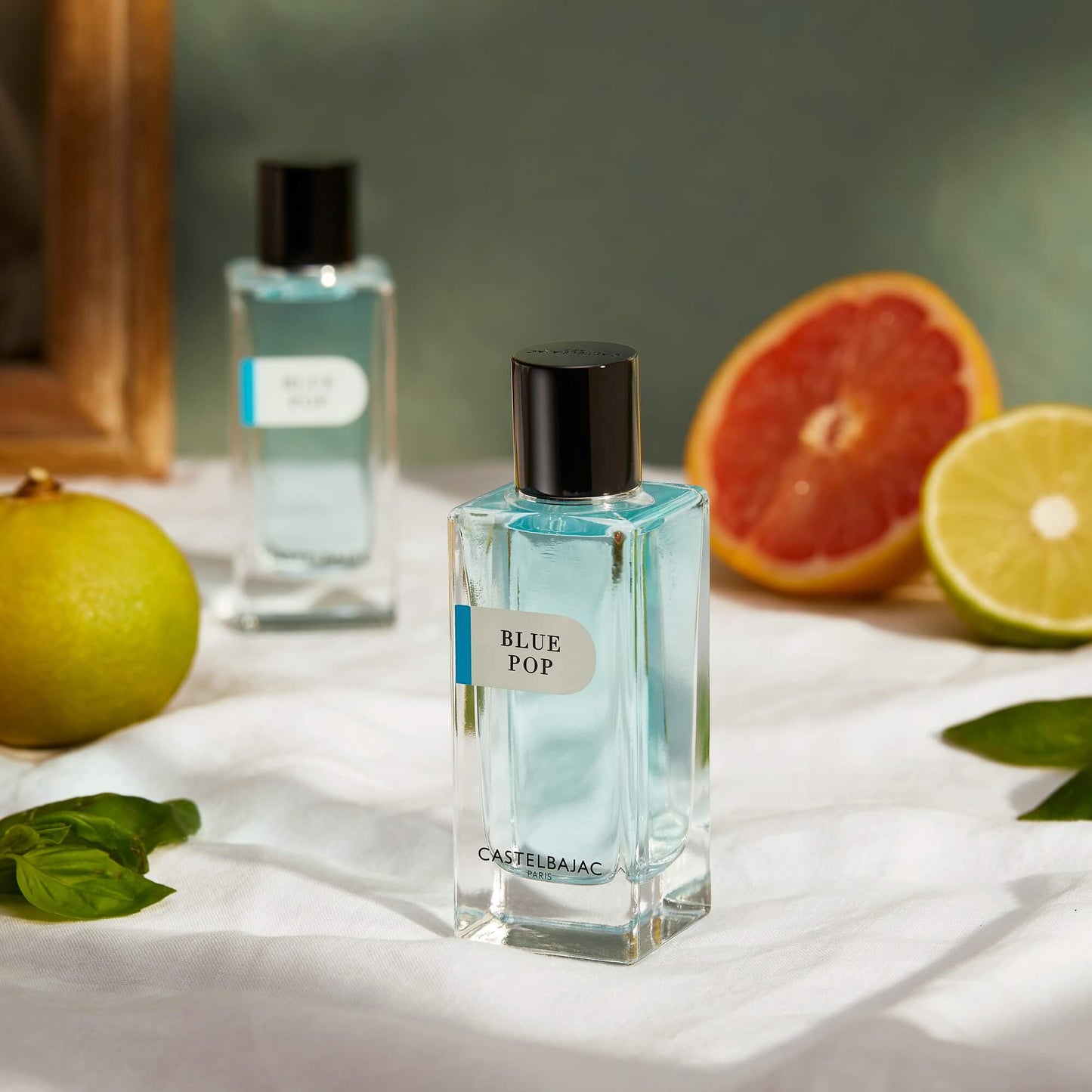 Castelbajac BLUE POP Eau de Parfum bottle with vibrant blue liquid, set against a backdrop of Mediterranean cliffs and turquoise waves