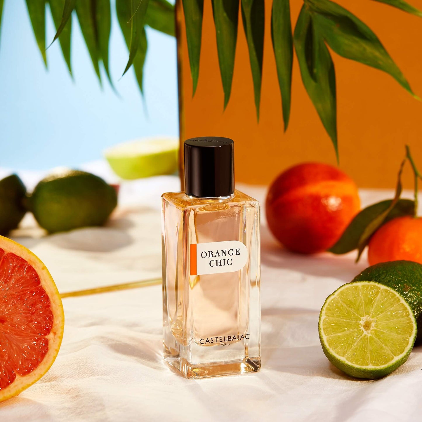 ORANGE CHIC Eau de Parfum bottle with vibrant orange liquid, glowing against a backdrop of Sicilian citrus groves and azure skies