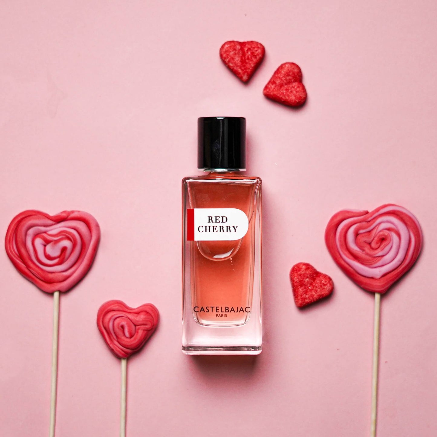 Castelbajac RED CHERRY perfume bottle with rich ruby liquid, glowing against a backdrop of cherries, pralines, and vanilla pods