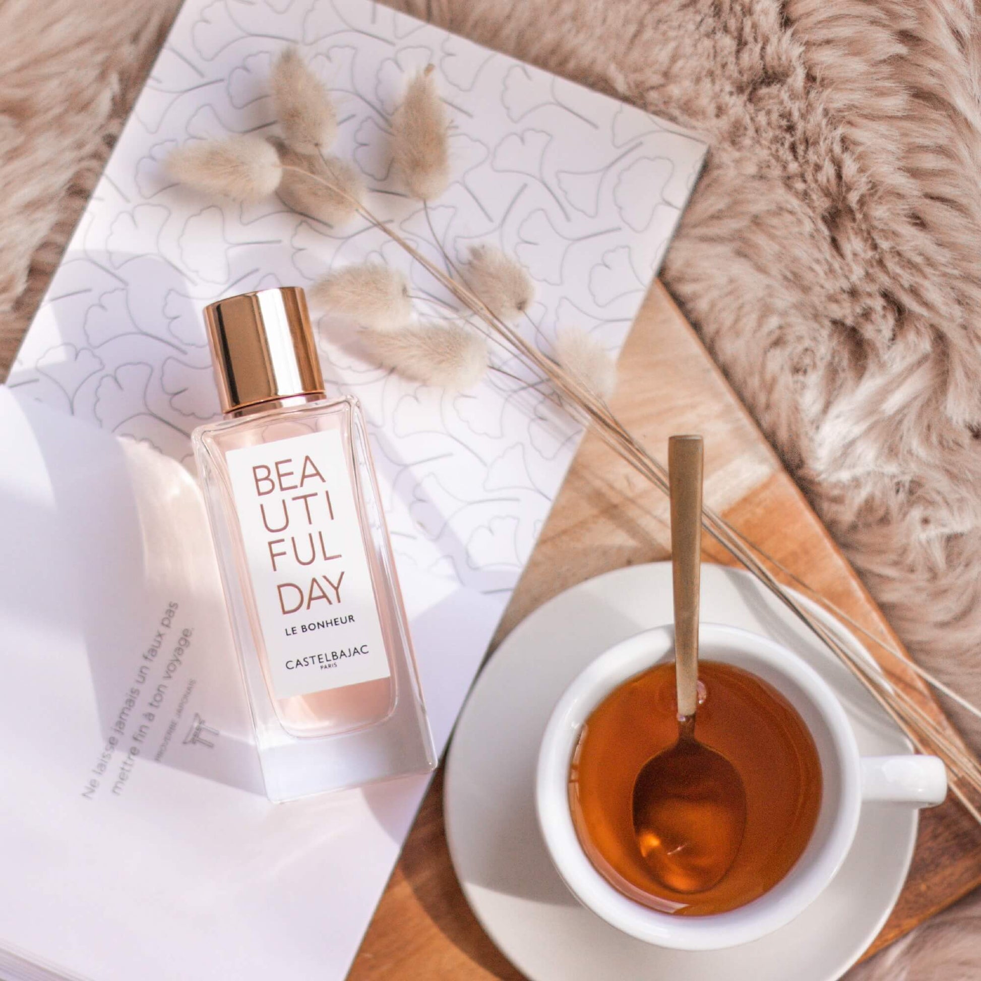 BEAUTIFUL DAY LE BONHEUR perfume bottle with golden-pink liquid, radiating vibrant energy against a sunlit, abstract backdrop